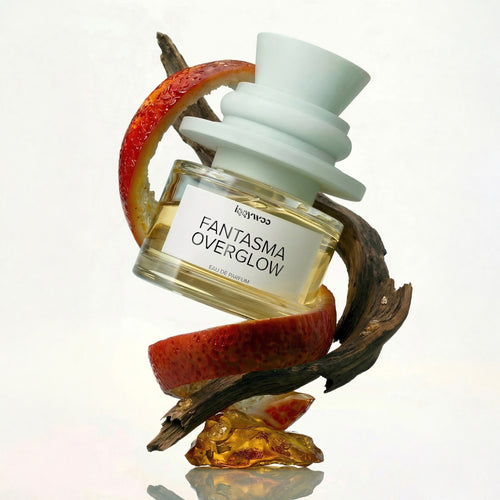 Perfume bottle labeled 'Fantasma Overglow' on a decorative stand with fruit slices.