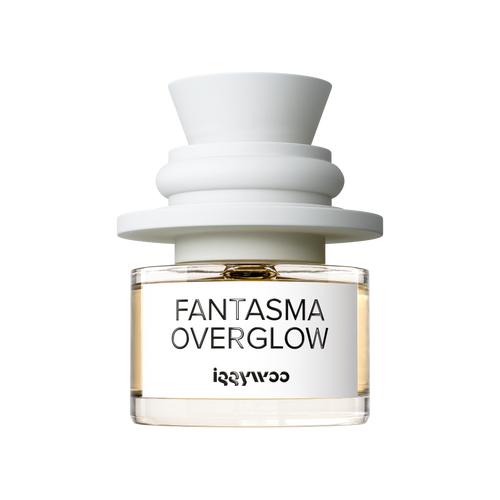 A clear glass perfume bottle with pale amber liquid, a white label reading 'FANTASMA OVERGLOW' and 'iggywoo', and a sculptural matte white cap, centered on a black background.